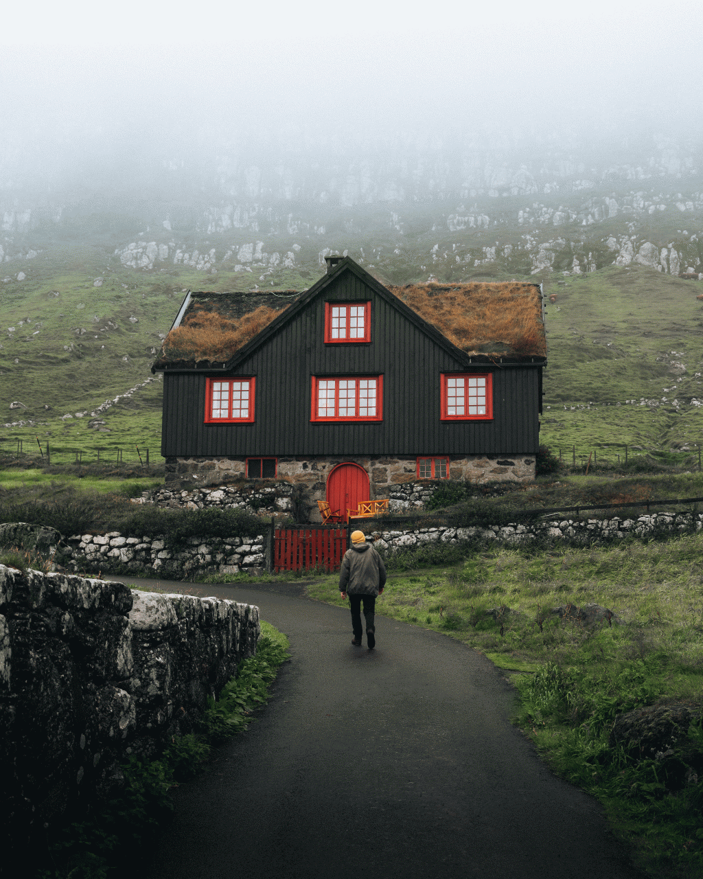 Man in front of turf-roofed house in, Kirkjubø, the Faroe Islands
